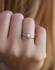 A delicate 14k yellow gold engagement ring, set with a center brilliant cut white diamond and smaller diamonds around it, in the shape of a geometric flower. 