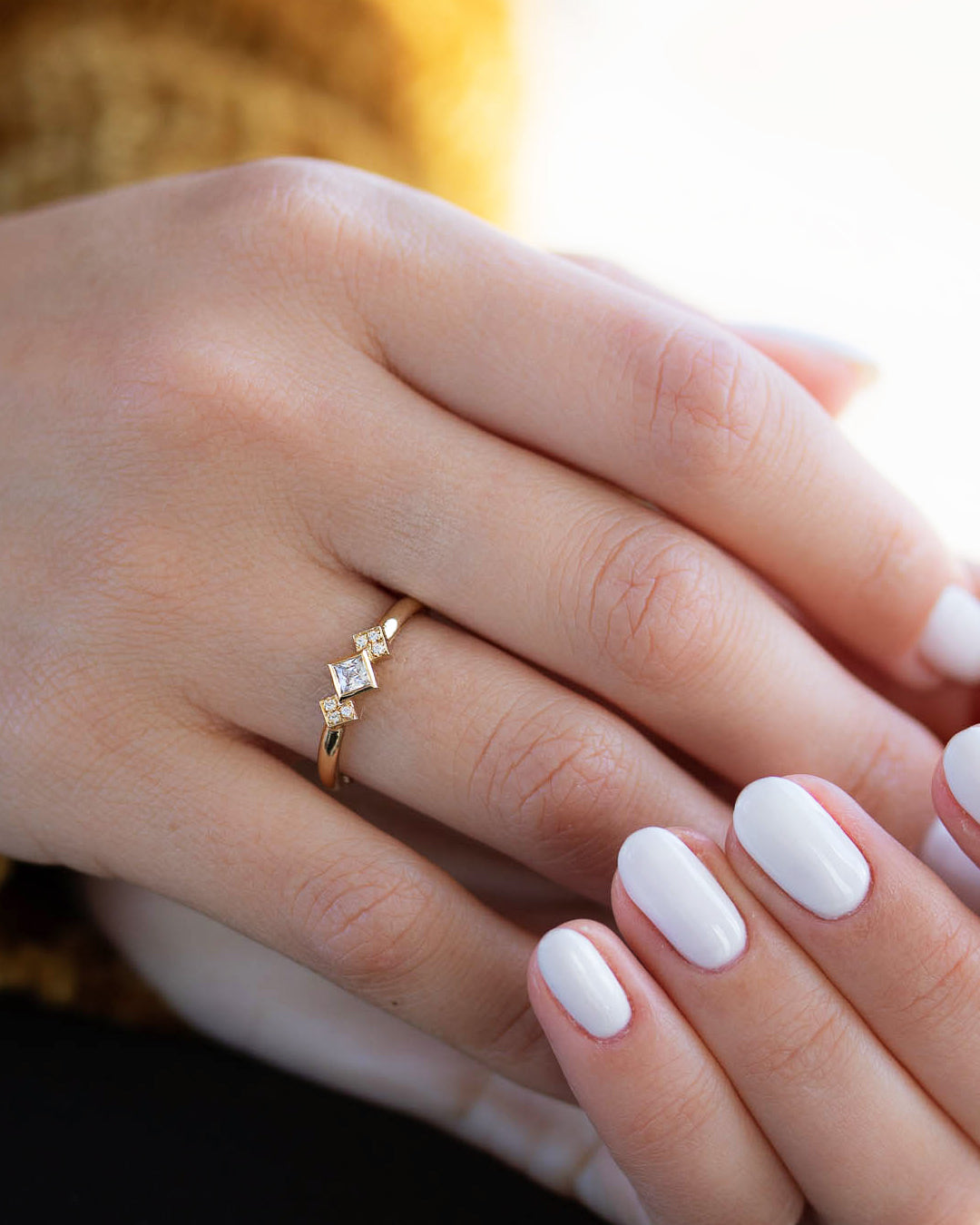 A delicate 14k yellow gold engagement ring, set with a center 0.25 carat princess cut white diamond, and three 0.01 carat brilliant cut white diamonds on each side.