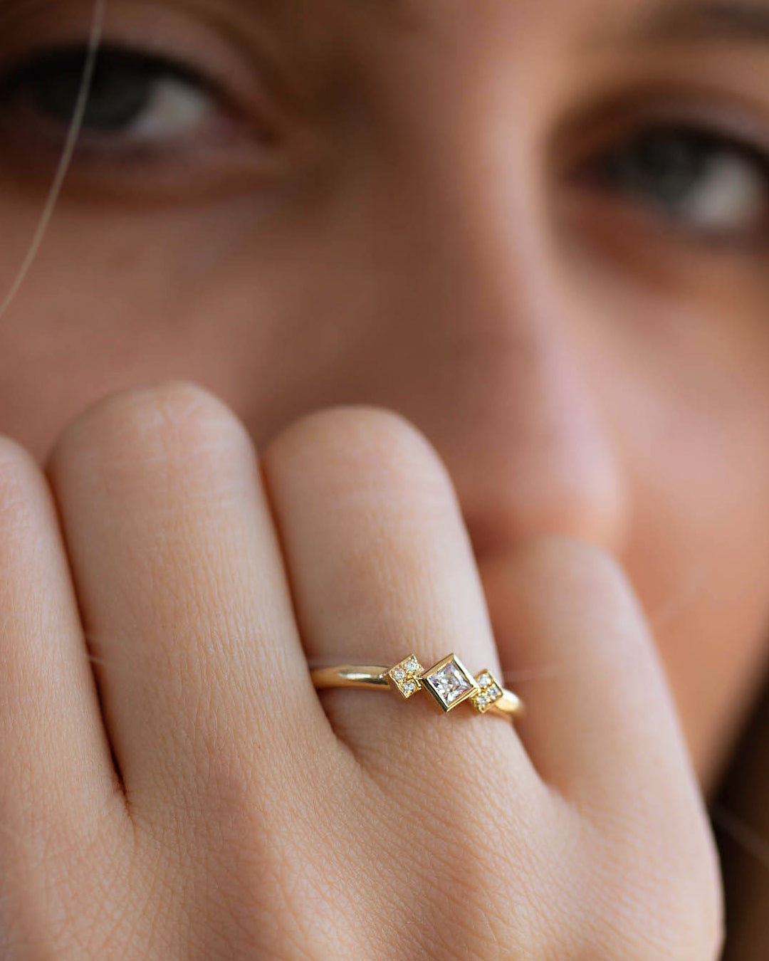 A delicate 14k yellow gold engagement ring, set with a center 0.25 carat princess cut white diamond, and three 0.01 carat brilliant cut white diamonds on each side.